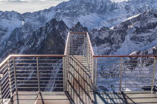 View across the High Tatra mountains from the observation deck at Lomnicky Peak, Slovakia. The day is sunny and clear and the mountains are covered in snow. The viewing platform is in the foreground, and the mountains are behind.