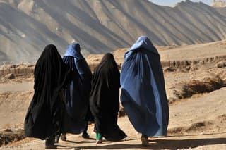 Bamyian city, Bamyian Province, Afghanistan - November 14, 2010: Four Afghan women in blue and black burqa walking on dirt path in barren land