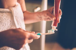 Close-up of senior woman's hands squeezing and applying toothpaste on toothbrush to brush her teeth