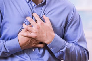 Mid-adult man clutching his chest in pain with a possible heart attack.  He wears a blue, button down dress shirt.  Heart disease.