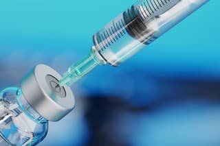 Medical disposable syringe for vaccine injection and glass vial on blue blur background.