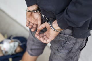 Drug dealer under arrest confined with handcuffs and hands at his back, standing next to a wall. Focus on the handcuffs chain