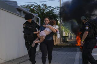 Izraelskí policajti evakuujú ženu s dieťom z miesta zasiahnutého raketami vystrelenými z pásma Gazy v izraelskom meste Aškelon