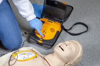 Performing a cardiopulmonary resuscitation (CPR) and using an AED (automated external defibrillator). Pushing the shock button. Demonstration on a CPR dummy