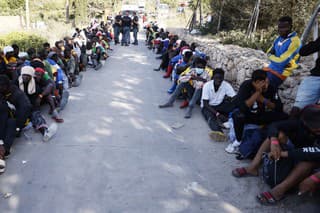 Ľudia sedia pred prijímacím centrom pre migrantov na sicílskom ostrove Lampedusa v piatok 15. septembra 2023. 