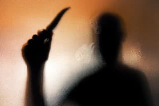 Colour backlit image of the silhouette of a man wielding a sharp knife in an aggressive way. The silhouette is distorted, and the arms elongated, giving an alien-like quality. The image is sinister and foreboding, with an element of horror. The image conveys a domestic violence, knife crime theme. Horizontal image with copy space.