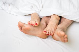 Feet of a couple in bed under the white blanket