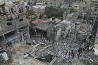 Palestínčania kráčajú okolo budov zničených počas izraelského bombardovania.