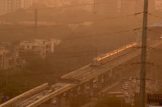 Evening shot of metro train on foggy delhi day. This is shot through electric wires that feed power to the railway lines. The metro is a power efficient public transport that will help solve the pollution and traffic congestion problems of Delhi Noida Gurgaon and other cities
