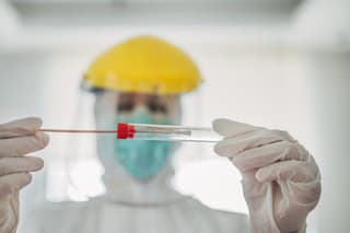 On woman, female doctor in protective suit holding and showing covid-19 tube test and sampling swab.