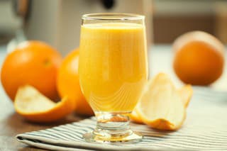 Glass of real freshly squeezed orange juice. Ambient light with juicer and oranges in background.