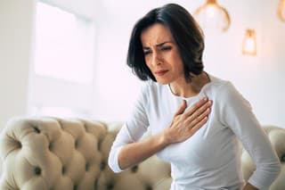 A stressed woman who is suffering from a chest pain and touching her heart area.