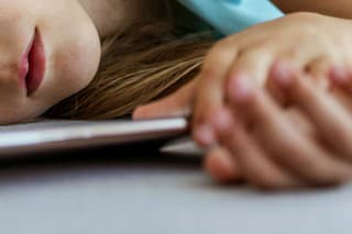 Cute youg girl sleeping in bed with smartphone. Front view of 7 years old child is lying on the sofa and holding smartphone with eyes closed.