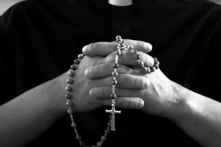 Silhouette of a praying priest with rosary beads in hands