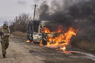 Ukrajinskí vojaci prechádzajú okolo dobrovoľníckeho autobusu, ktorý horí po zásahu ruského dronu.