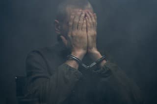 A suspect in handcuffs closing his face with hands in a dark fogged room