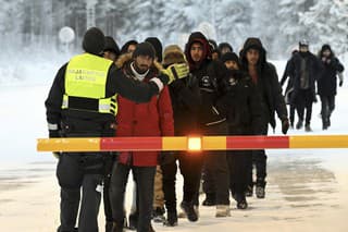 Príslušník fínskej pohraničnej stráže hovorí s migrantmi, ktorí prichádzajú na medzinárodnú hranicu medzi Fínskom a Ruskom