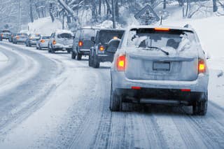 A line of cars slowly driving on a snowy, icy road. Entire image is monochrome blue-ish except the taillights, which are glowing red and yellow.