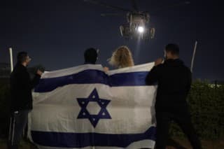 Ľudia držiaci izraelskú vlajku sledujú prílet helikoptéry prevážajúcej izraelských rukojemníkov prepustených Hamasom.