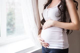 Pregnant woman standing by the window. Close up
