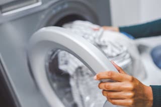Closeup shot of an unrecognisable woman using a washing machine to do laundry at home