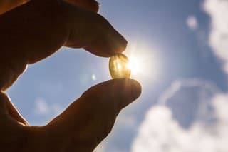 Vitamin D keeps you healthy while lack of sun. Yellow soft shell D-vitamin capsule against sun and blue sky on sunny day. Cure concept.