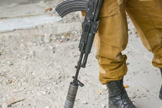 A man in overalls holds a Kalashnikov assault rifle with a silencer in his hand, close-up. Small arms of the Russian special forces.