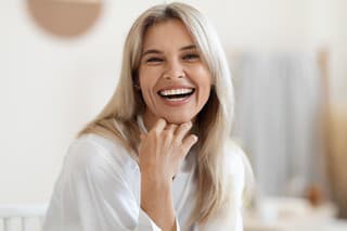 Portrait of beautiful middle aged woman touching her face and laughing, enjoying her smooth face skin after using anti-aging cosmetics in the morning, bathroom interior, copy space