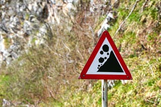 A sign warning of rock falls along a highway in the mountains.