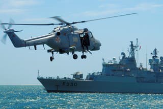 Setubal, Portugal: Portuguese Navy Super Lynx Mk.95 helicopter with diver on the door, approaching frigate F330, NRP Vasco da Gama, built by Westland Helicopters. Portuguese Naval Aviation. Two Lynx can be operated from the flight deck of a Vasco da Gama-class frigate.