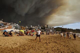Dovolenkári hrajú paddleball na pláži, v pozadíhustý čierny dym z neďalekých lesných požiarov v čilskom meste Vina del Mar v piatok 2. februára 2024.