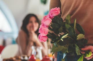Close up shot of unrecognizable male holding a bouquet of roses behind his back, about to surprise his girlfriend.