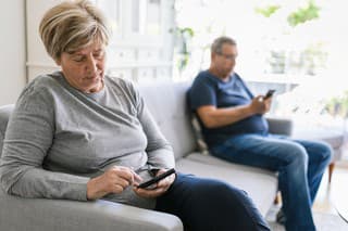 Senior couple sitting on couch and using their mobile phones at home