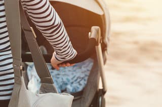 Mother walking with baby in a stroller on bright sunny spring day