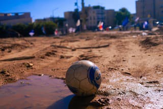 Sderot, Israel – February 07, 2024: A soccer ball left in the dirt of Sderot, Southern Israel, in the background is former police station - now a memorial site.