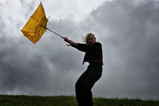 Standing outdoors in a thunderstorm, a young woman struggles as a gale-force wind blows her umbrella inside out.