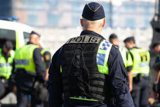 Stockholm, Sweden - August 28, 2020: A Swedish policeman standing alone with his back turned watching his fellow police officers working in front of him.