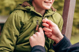 cropped shot of father fastening jacket of cute smiling little son in park