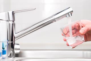 Filling glass with tap water. Modern faucet and sink in home kitchen. Man pouring fresh drink to cup.