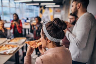 Group of male and female coworkers having lunch break eating pizza together in office