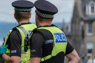20th June 2020: Rear view of two male Police Scotland officers on duty in Edinburgh, during a Black Lives Matter demonstration in St Andrew Square, during the Coronavirus pandemic. One officer is wearing protective rubber gloves. Both officers are wearing high visibility jackets with their police uniforms, with the police logo on the back. They are standing looking down the street, keeping surveillance of the crowds. They have handheld radios attached to their jackets to communicate with colleagues.