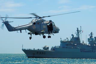 Setubal, Portugal: Portuguese Navy Super Lynx Mk.95 helicopter with diver on the door, approaching frigate F330, NRP Vasco da Gama, built by Westland Helicopters. Portuguese Naval Aviation. Two Lynx can be operated from the flight deck of a Vasco da Gama-class frigate.
