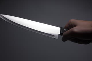 Male hand holding large, sharp, shiny kitchen knife. Isolated on dark background. Photo is taken with dslr camera indoors.