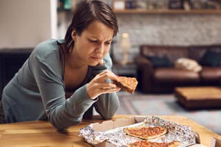 Young unhappy woman eating pizza due to her depression at home.