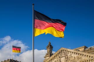 German flags waving in the wind at famous Reichstag building, seat of the German Parliament (Deutscher Bundestag), on a sunny day with blue sky and clouds, central Berlin Mitte district, Germany.