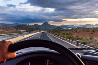 View from the driving position of a truck of the highway and a landscape of mountains in the background at dawn.