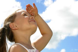 Photo of a young girl looking up into the blue sky and puffy clouds.