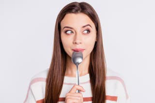 Very hungry lady holding spoon into mouth, dream of tasty meal wear striped pullover isolated white background