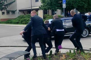 Zraneného premiéra držia ochrankári a nakladajú ho do auta.