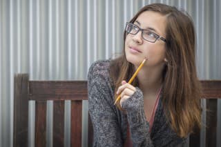 Pretty Young Daydreaming Female Student With Pencil Sitting on Bench Looking to the Side.